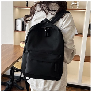 Rear view of minimalist black nylon backpack with padded straps shown in a room setting