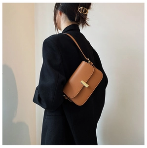 Brown leather saddle bag with golden clasp worn over a black blazer by a model