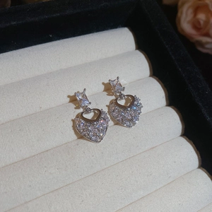 Macro shot of silver heart-shaped zircon earrings placed in a beige velvet jewelry box