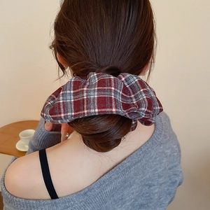 Detail of a large red plaid fabric scrunchie styled on a woman's low ponytail