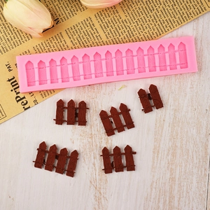 Pink silicone garden fence fondant mold with brown chocolate fence pieces on wooden desk