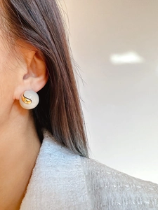 Detail of round handmade enamel stud earrings in beige and gold on a model ear