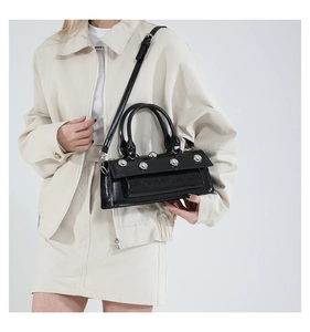 Detail of black patent leather baguette bag with silver rivets and adjustable strap