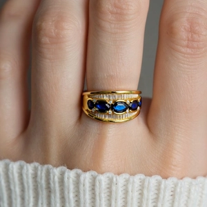 Detail of 18K gold ring with deep blue oval gemstone and white zircon on model hand