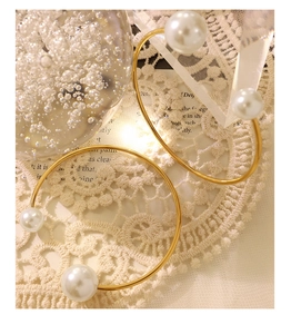Detailed view of elegant gold bangle with white pearls on a lace and vintage book background