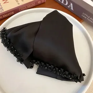 Elegant black satin bow hair claw clip with crystal beads on a white ceramic plate