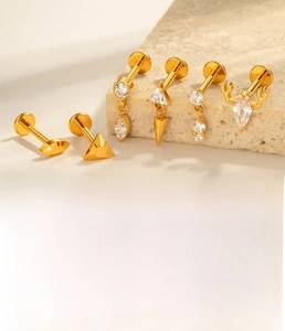 G23 titanium labret studs with gold zircon designs on a beige stone surface