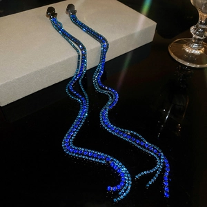 Macro detail of long snake-shaped tassel earrings with blue rhinestones on dark metal