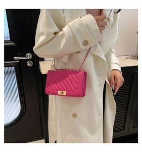 Detail of rose red quilted crossbody bag with gold chain strap on white coat