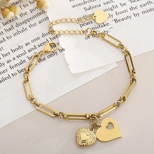 Detail of gold paperclip chain bracelet featuring embossed and hollow heart charms