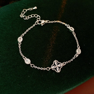 Detailed view of silver adjustable bracelet with zircon clover pendant on green velvet