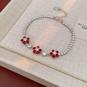 Detail of silver flower bracelet with red and white zircon stones on a woven texture