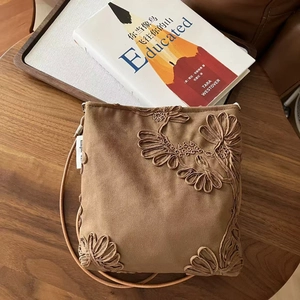 Détail de broderie florale sur sac bandoulière en daim marron avec livres