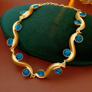 Detail of vintage gold necklace featuring wavy links and embedded round blue gemstones