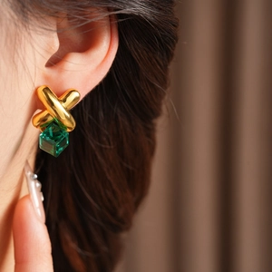 Close-up of model wearing gold X-shaped earrings with a green square gemstone