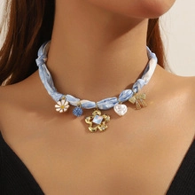 Close-up of a blue fabric cord necklace with daisy, heart, and bow pendants on a model