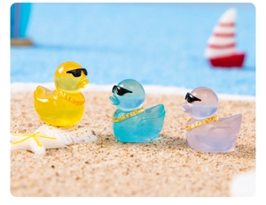 Close-up of colorful glowing resin ducks with sunglasses on sand for DIY scenery
