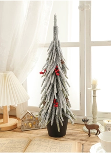 Miniature snow-flocked green Christmas tree with red berries on a wooden desk setup
