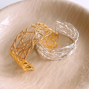 Close-up of hollow interwoven gold and silver cuff bracelets on a ceramic tray