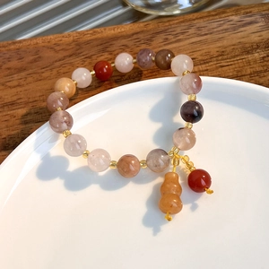 Macro view of multi-colored jade gourd bracelet with gold spacers on a ceramic dish