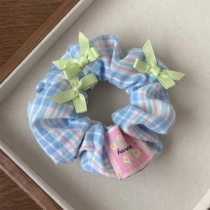 Close-up of blue plaid scrunchie with green bows and floral hand-stitched label