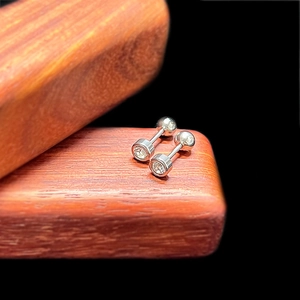 Macro view of silver barbell ear studs with bezel-set round cubic zirconia stones
