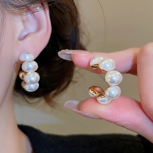 Detailed close-up of C-shaped gold-plated earrings with five white round pearls