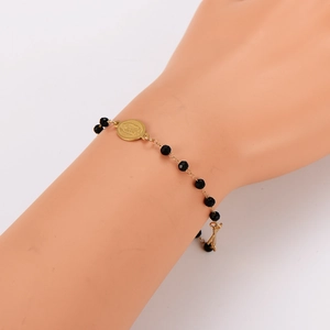 Golden beaded bracelet with black faceted beads and oval virgin mary pendant on a model