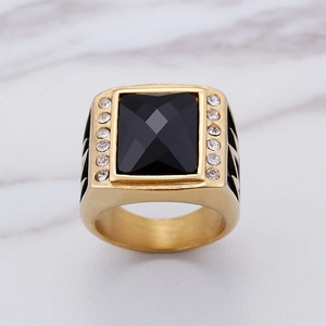 Detail eines quadratischen Goldrings mit großem schwarzem Stein und seitlichen Kristallen