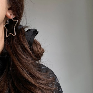 Close-up of a silver-colored star-shaped large hoop earring worn on a model's ear