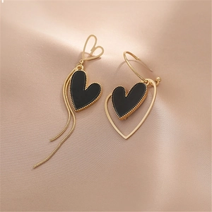 Detail of asymmetric gold earrings with black heart charms and delicate tassel chains
