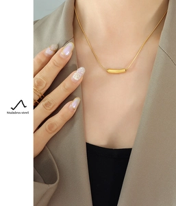 Détail d'un collier sourire en acier inoxydable doré avec pendentif tube sur un mannequin