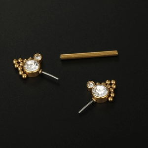 Golden cubic zirconia ball nipple ring studs with clear crystals on dark textured surface