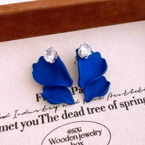 Macro detail of luxury flower drop earrings with blue petals and sparkling clear gemstone