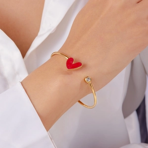 Detail of gold open bangle featuring a red enamel heart and a small sparkling crystal stone
