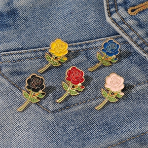 Set of five colorful rose enamel pins in yellow, blue, black, red, and pink on denim