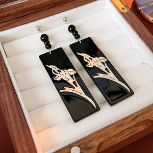 Macro detail of rectangle black earrings with orchid pattern in a wooden jewelry box