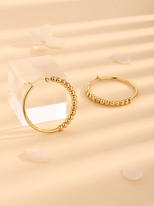 Polished gold-tone hoop earrings with continuous bead accents on a textured light background