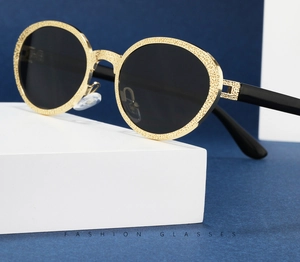 Detail of gold metal oval frame with intricate engraved texture and black sunglasses lenses