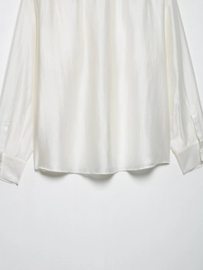 Detailed macro view of the pearl white satin blouse showing smooth curved hem and buttoned cuffs