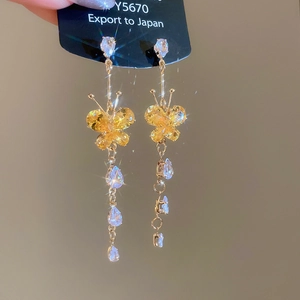 Detailed close-up of golden butterfly drop earrings with yellow crystals and tassels