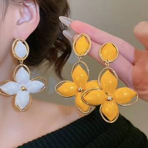 Détail de boucles d'oreilles fleurs en émail blanc et jaune portées par un mannequin en gros plan
