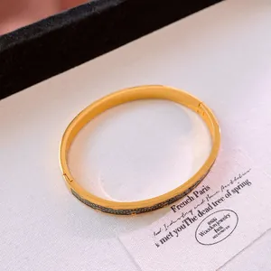Gros plan du bracelet ovale en acier doré avec motif œil grec sur fond blanc texturé