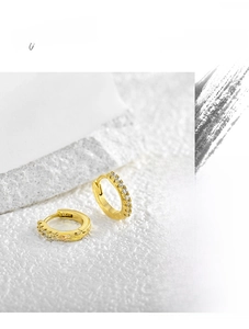 Close-up of gold huggie earrings with micro-paved cubic zirconia on stone background