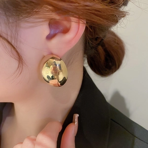 Close-up of model wearing gold irregular teardrop metal earrings with a glossy finish