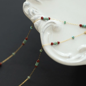 Macro shot of turquoise and burgundy glass beads on a gold chain over a white plate