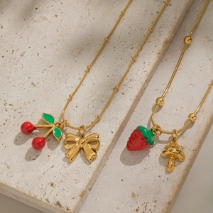 Detail of gold necklaces with cherry and strawberry enamel charms on a stone surface