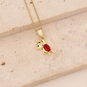 Close-up of golden bear pendant with red zircon inlay on textured stone background