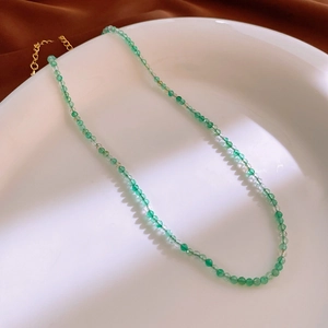Close-up of translucent green beaded necklace with gold lobster clasp on white ceramic plate