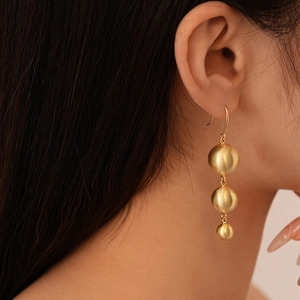 Detail of matte gold triple ball drop earrings worn by a model in a close-up side view